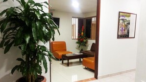 Una sala de estar con una planta grande en maceta, dos sofás naranja, una mesa de centro y un cuadro enmarcado en la pared.