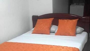 Una cama individual con colcha y almohadas naranjas, cabecera de madera oscura y paredes blancas.