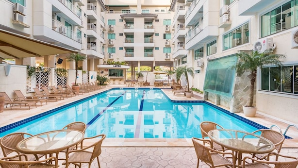 A swimming pool with lounge chairs and tables, surrounded by multi-story buildings with balconies and air conditioning units. - Aluguel Apartamento 1 quarto Summer Beach 076A (Bombinhas)