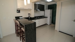 A modern kitchen with a central island, white cabinetry, and a built-in stove. - Aluguel Apartamento 1 quarto Summer Beach 076A (Bombinhas)
