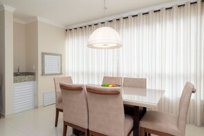 Un comedor con una mesa y sillas, una lámpara colgante y un ventanal con persianas verticales.