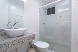 Un baño con lavamanos blanco, inodoro y ducha con mampara de vidrio.