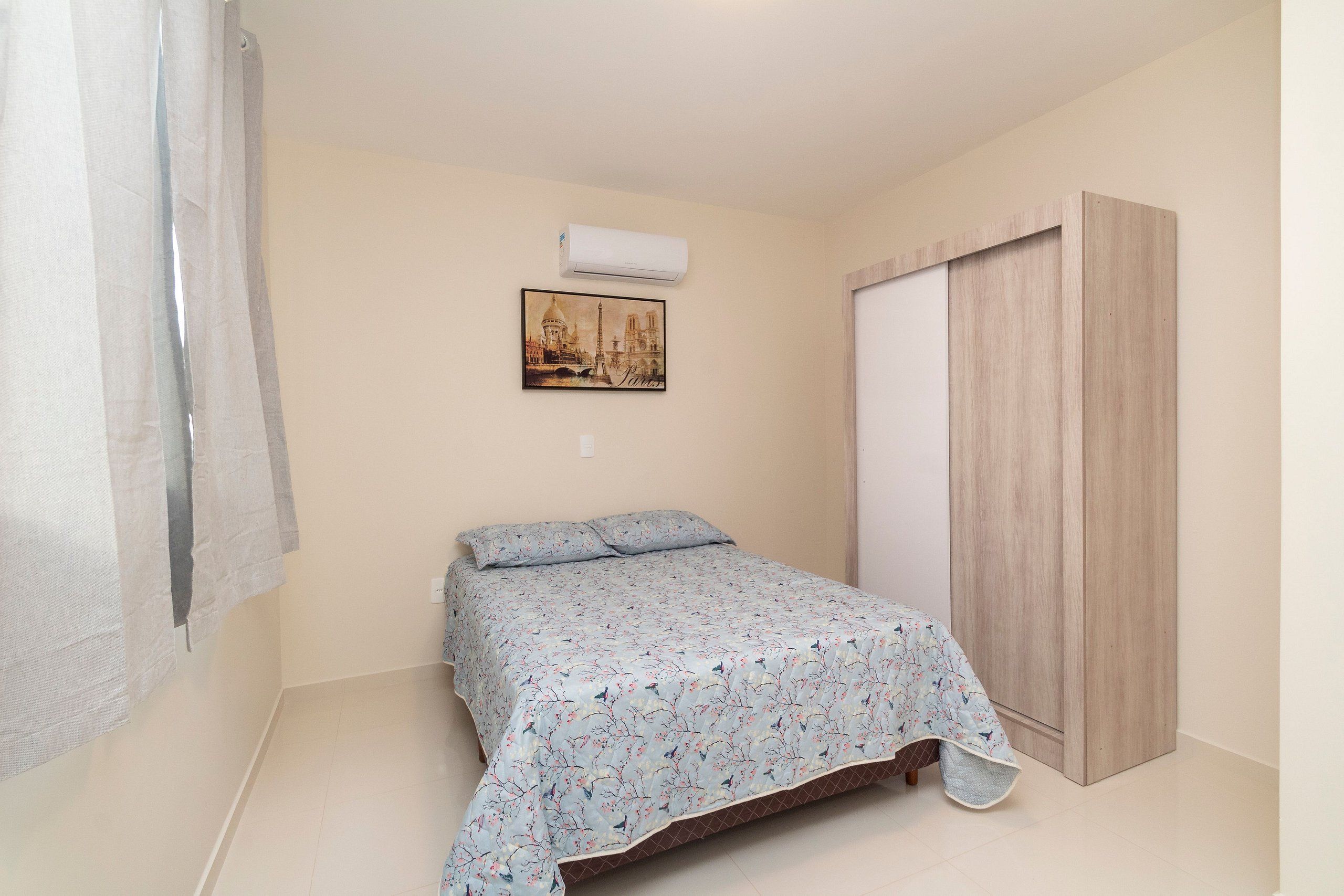 Une chambre à coucher avec un lit, un climatiseur fixé au mur, une image de Paris et une armoire en bois.