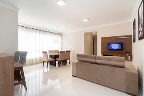 Una sala de estar moderna con sofá, mesa de comedor, sillas y televisor de pantalla plana montado en la pared.