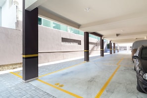 Un parking avec des piliers en béton, des lignes jaunes et une voiture garée sur le côté droit.