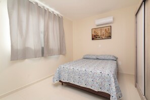 Un dormitorio con cama, ventana con cortinas, equipo de aire acondicionado y un cuadro en la pared.
