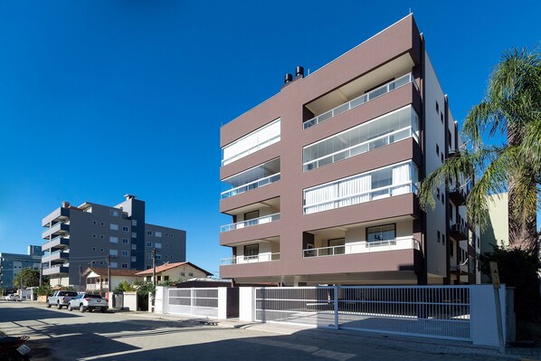 Un edificio residencial de varios pisos con balcones y una entrada protegida por una reja.
