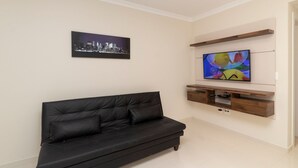 Una sala de estar moderna con un sofá de cuero negro, un televisor montado, una obra de arte con un paisaje urbano y estanterías de madera.