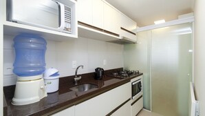 A compact kitchen with white cabinets, a stainless steel sink, a microwave, a kettle, and a water dispenser.