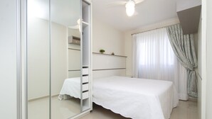 A bedroom with a bed, a wardrobe, a ceiling fan, and a window with curtains.