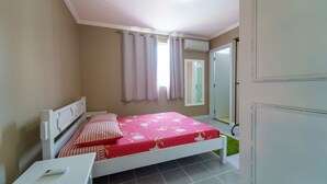 Un dormitorio con cama, mesita de noche, ventana con cortinas y aire acondicionado.