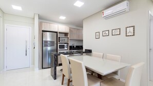 Een moderne keuken met een geïntegreerde koelkast, magnetron en fornuis. Er is een eethoek met een witte tafel en stoelen.