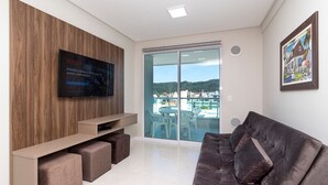 Een moderne woonkamer met een flatscreen televisie, een houten accentmuur, een bank en een balkon met uitzicht op de stad.