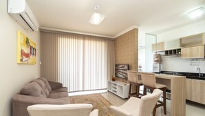 Een moderne woonkamer met een bank, stoelen, een televisie en een keuken met kasten en een fornuis.
