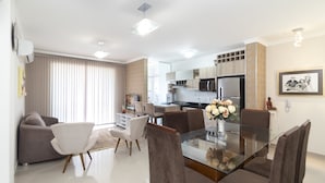 Een moderne keuken met inbouwapparatuur, een eethoek met een glazen tafel, en een woonkamer met een bank en een televisie.