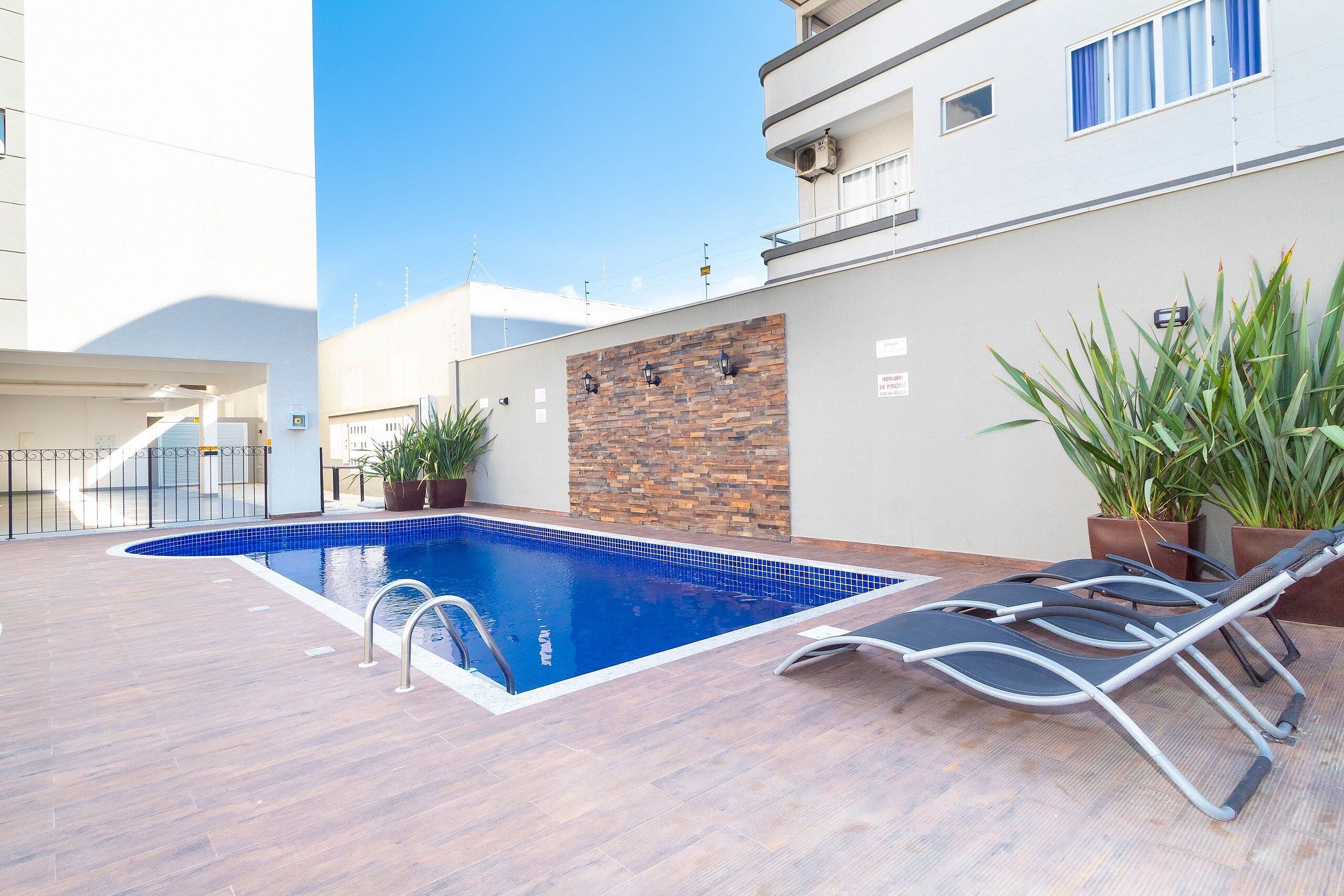 Una piscina con cubierta de madera, sillas de descanso y plantas en macetas.