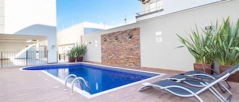 Una piscina con cubierta de madera, sillas de descanso y plantas en macetas.