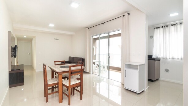 Una sala moderna con una mesa de comedor, sillas, un sofá, una pequeña cocina y un ventanal corredero que da a un balcón.
