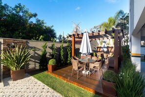 Une terrasse avec une plateforme en bois, du mobilier d’extérieur et une pergola surmontée d’un parasol blanc.