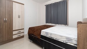 Un dormitorio con cama, armario y ventana con cortinas.