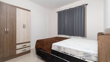 Quarto com cama, guarda-roupa e janela com cortinas.