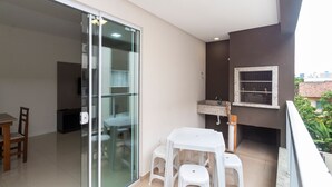 Un balcó amb una taula blanca i tamborets, una porta corredissa de vidre i una petita cuina amb un rentaplat i una finestra.
