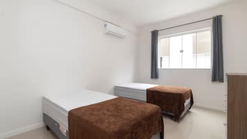 Quarto com duas camas, um guarda-roupa e uma janela com cortinas.