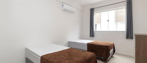 A room with two beds, a wardrobe, and a window with curtains.