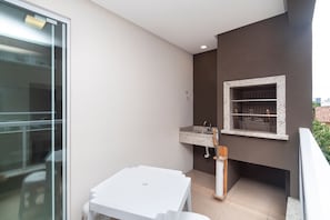 Un balcon avec une table blanche, un petit lavabo et une fenêtre avec une étagère.