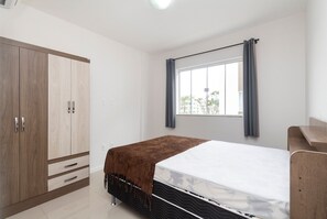 Une chambre à coucher avec un lit, une armoire, une fenêtre avec des rideaux et une vue sur l’extérieur.