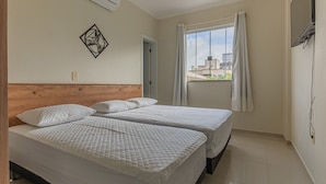 Une chambre d’hôtel avec deux lits, une tête de lit en bois, une fenêtre avec des rideaux et un climatiseur fixé au mur.