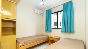 A small, clean room with a single bed, a wooden wardrobe, a bedside table, and a window with curtains. - Aluguel Apartamento 3 quartos 1 suite 100m Mar 427 (Bombinhas)