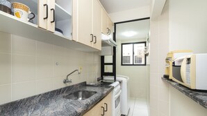 A compact kitchen with a granite countertop, a built-in sink, a white stove, and a microwave. - Aluguel Apartamento 3 quartos 1 suite 100m Mar 427 (Bombinhas)