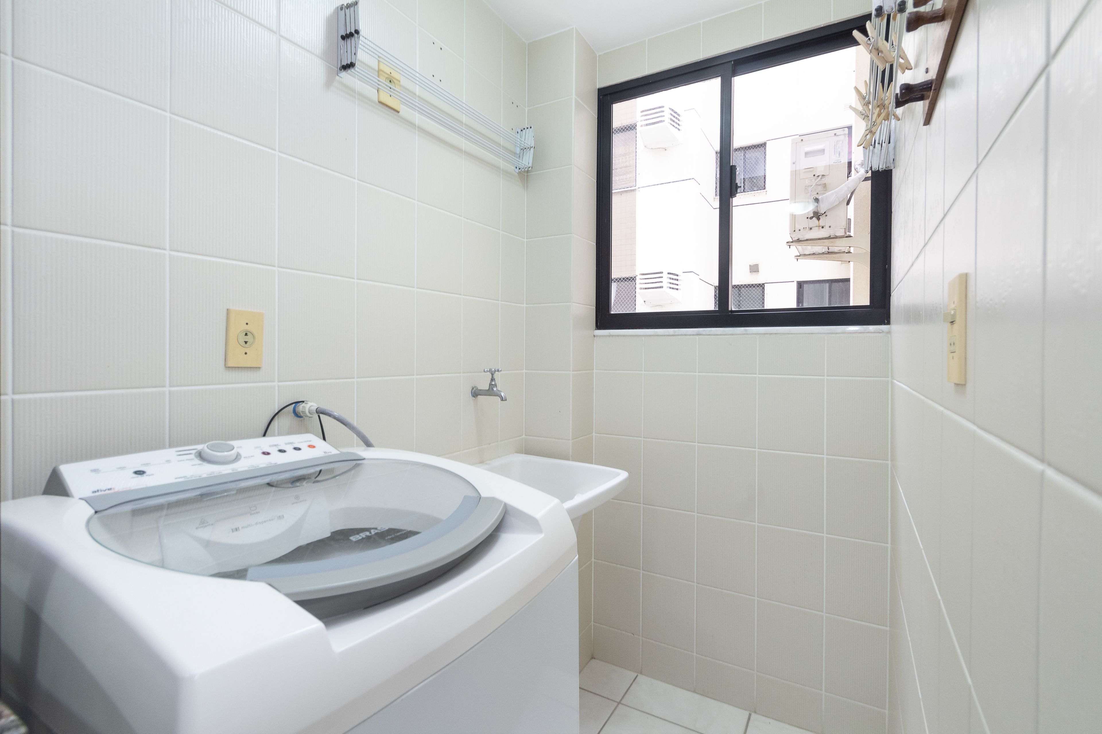 Une salle de bain moderne équipée d’un lave-linge intégré, d’une baignoire et d’une fenêtre donnant sur des immeubles.