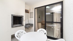 A small balcony with a round table and two chairs, a sink, and a sliding glass door leading to an interior room. - Aluguel Apartamento 3 quartos 1 suite 100m Mar 427 (Bombinhas)