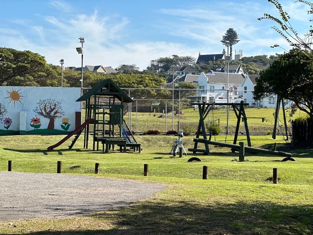 Un parque infantil con tobogán y columpios, rodeado por una cerca y un mural.