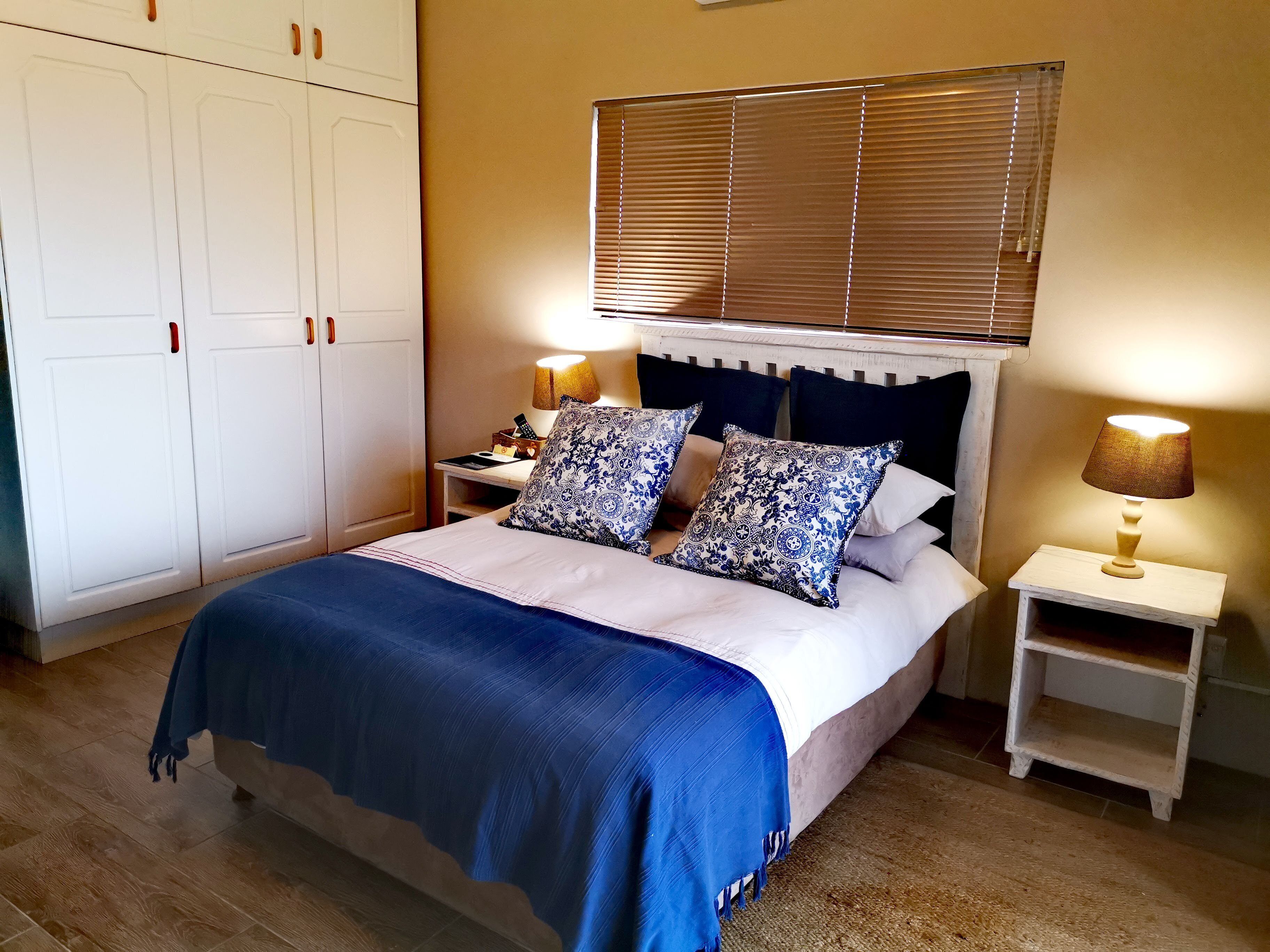 A bedroom with a bed, two bedside tables, a nightstand, a wardrobe, and a window with blinds.