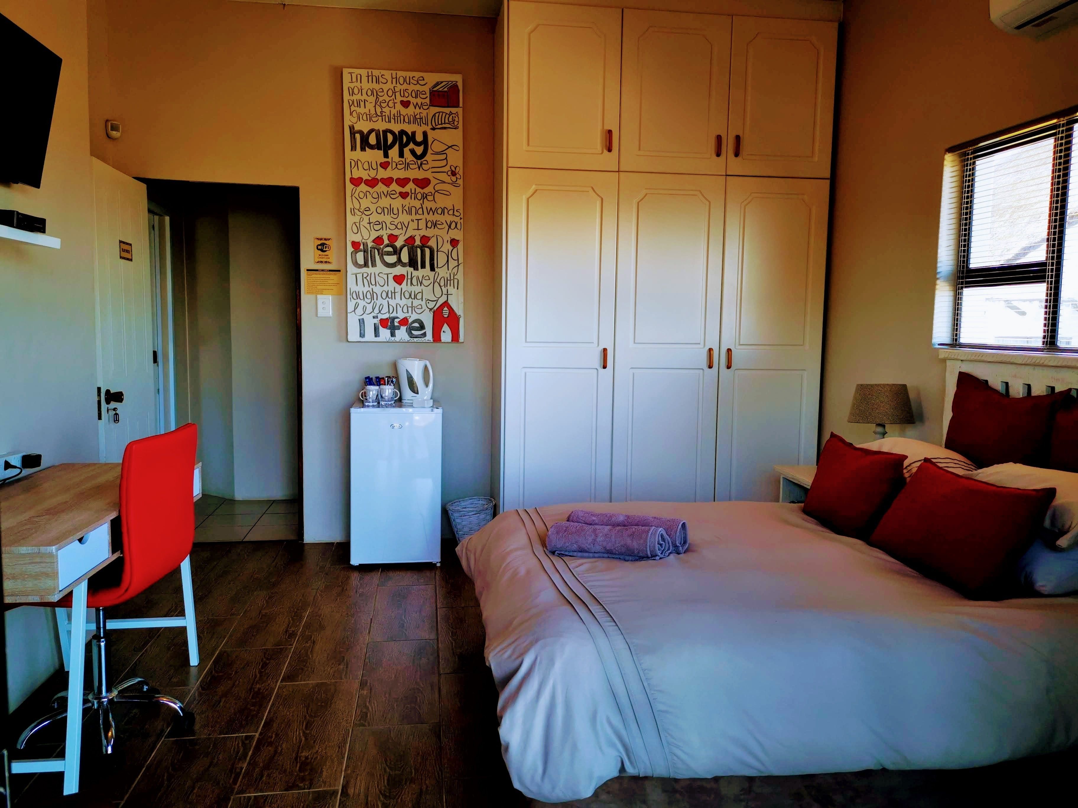 A bedroom with a bed, a desk with a chair, a wardrobe, and a poster on the wall.
