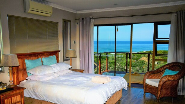 A bedroom with a large bed, a chair, and a view of the ocean. - Cove View Bed & Breakfast (East London)