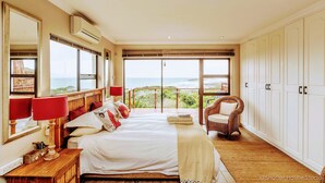 A bedroom with a large bed, a chair, and a view of the ocean. - Cove View Bed & Breakfast (East London)