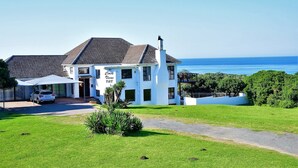 A white building with a tiled roof, a covered car parking area, and a grassy lawn in front. - Cove View Bed & Breakfast (East London)
