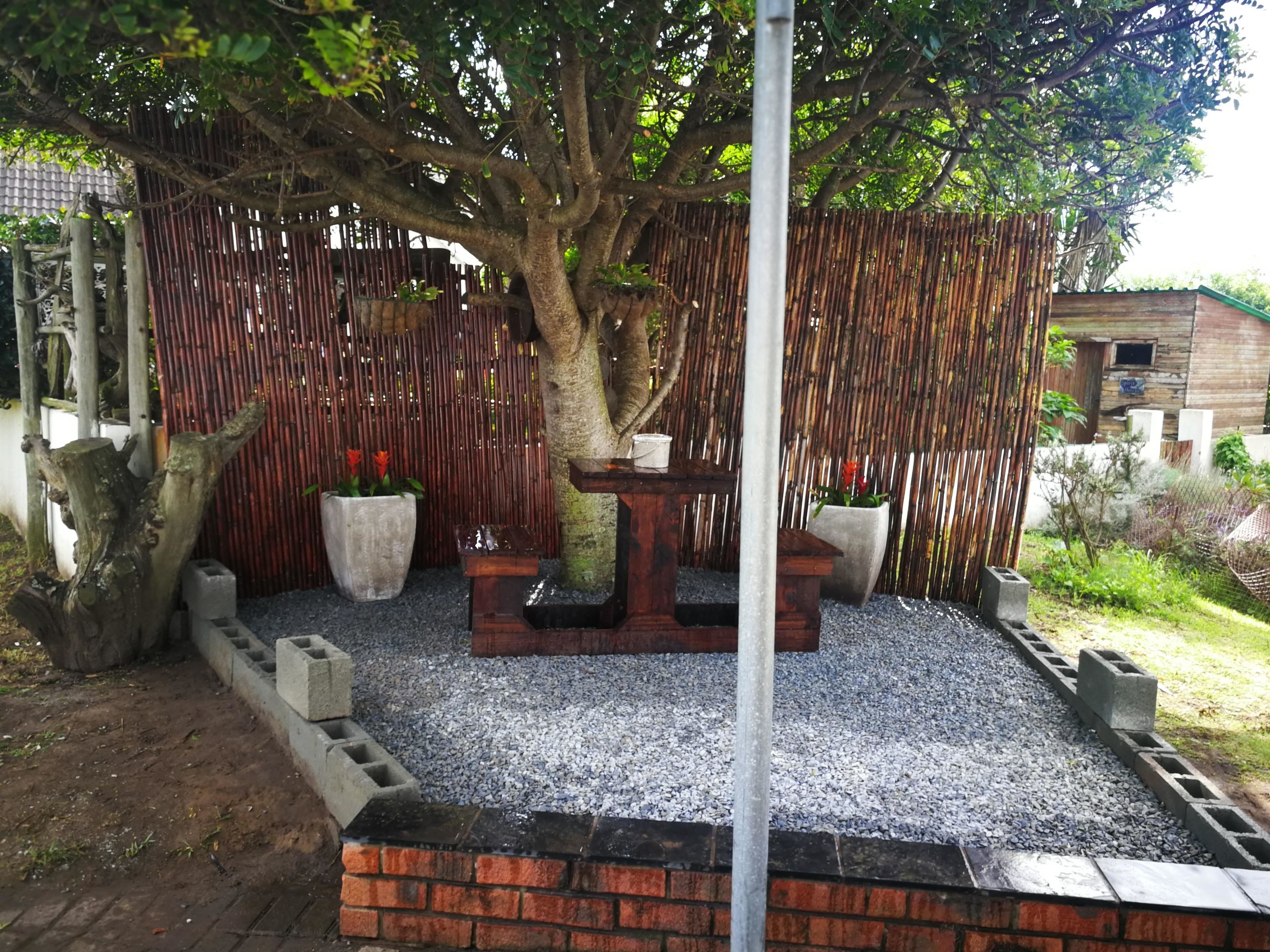 A garden area with a wooden fence, a large tree, and a seating area with planters.