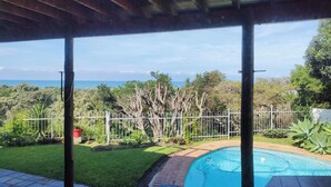 A covered outdoor area with a swimming pool, surrounded by greenery and a view of the ocean. - Cove View Bed & Breakfast (East London)