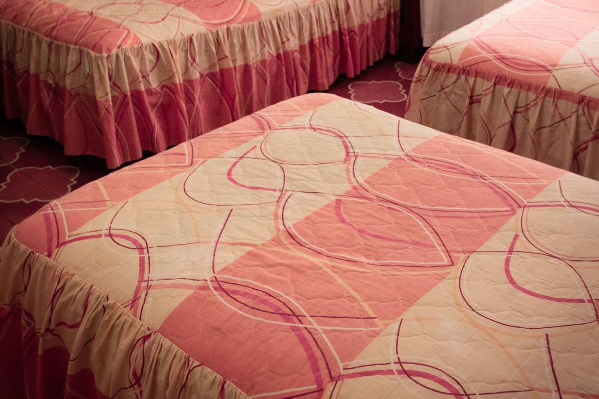 A room with two single beds, each with a patterned bedspread. The room has a wooden headboard and a window with curtains.