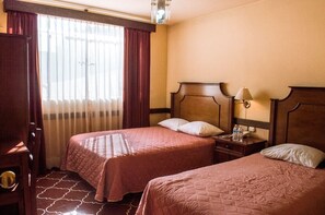 A hotel room with two beds, a nightstand, a lamp, and a window with curtains. - Hotel de Don Pedro (Guatemala City)