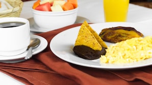 A breakfast setting with a plate of eggs, plantains, and a bowl of fruit. - Hotel de Don Pedro (Guatemala City)