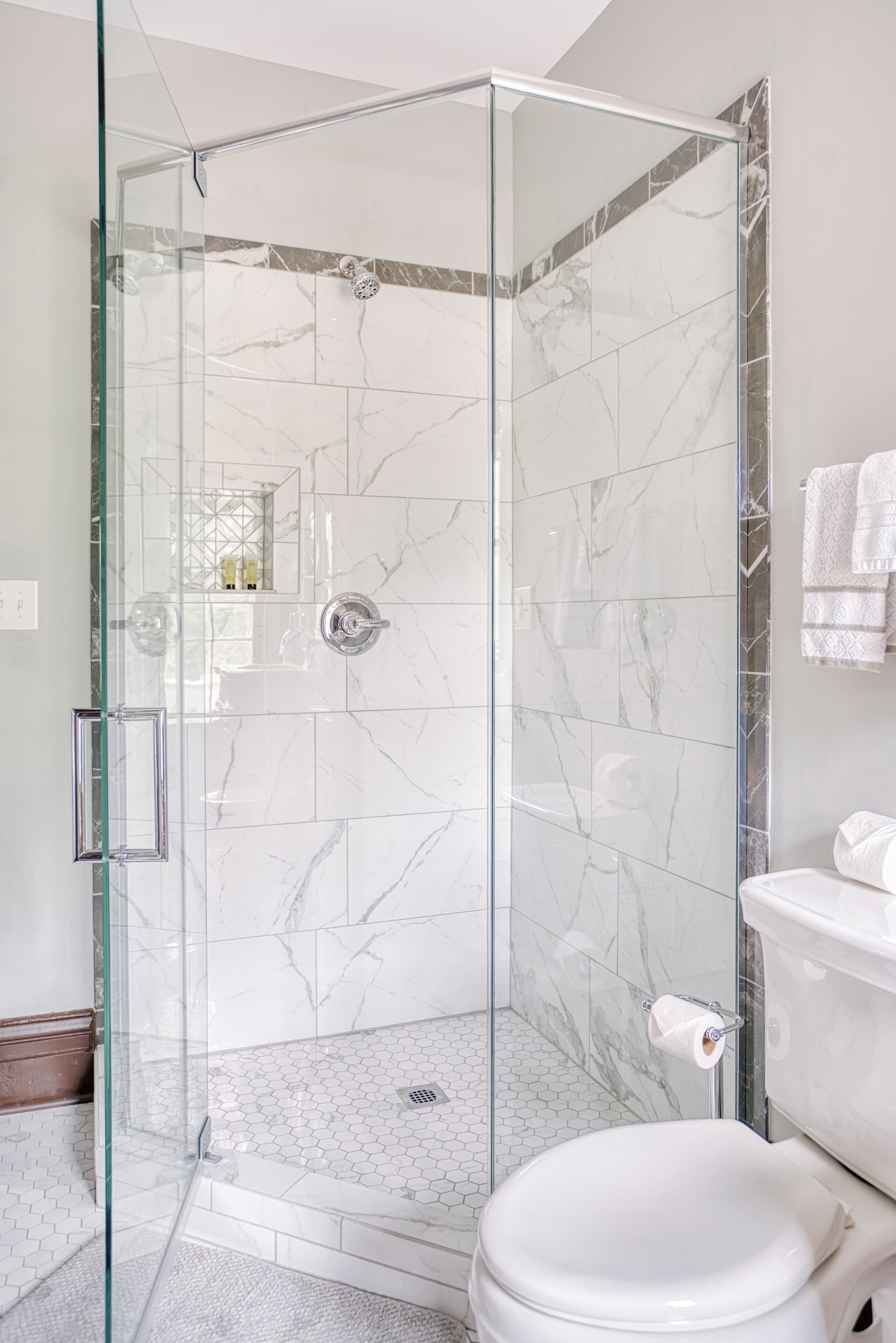 Ein modernes Badezimmer mit einer gläsernen Dusche, weißen Marmorfliesen und einer weißen Toilette.