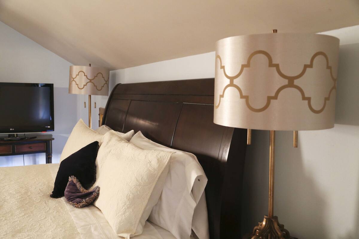 Ein Hotelzimmer mit einem großen Bett, einem Flachbildfernseher, einem dunklen Holz-Kopfteil und zwei Lampen mit gemusterten Schirmen.