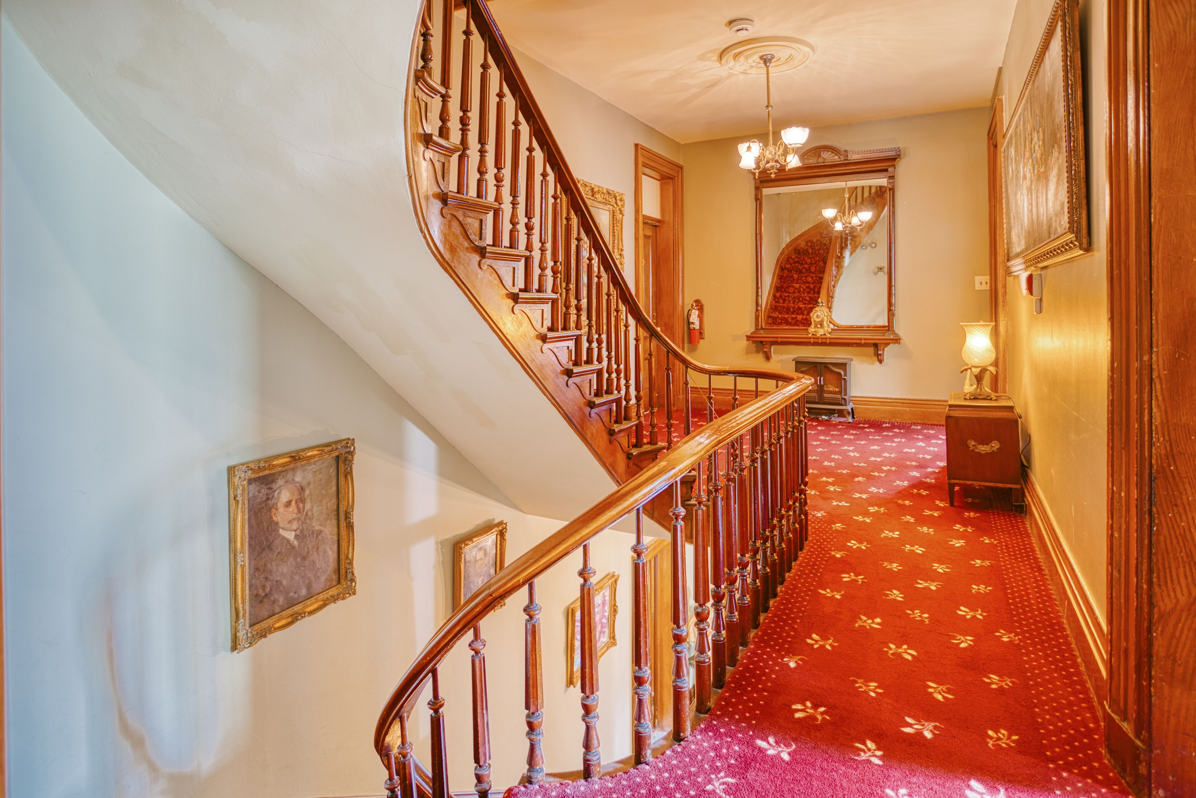 Un magnifique escalier orné de boiseries sculptées et recouvert d’une moquette rouge.