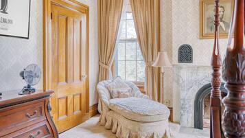A bedroom with a wooden door, a bed with a white bedspread, a nightstand, a lamp, and a fireplace.